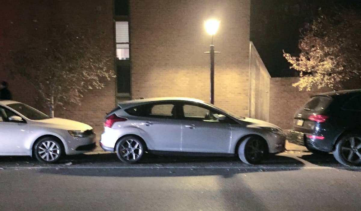 Silver car parked on street, very close to cars in front and behind.